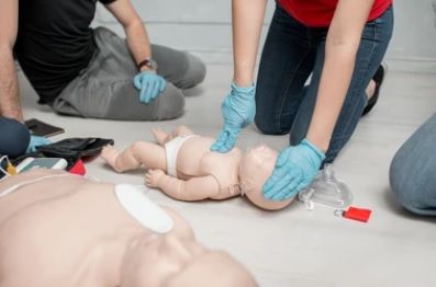 Mensen met blauwe handschoenen oefenen reanimatie bij een baby op een pop tijdens een trainingssessie.