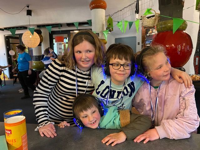 Vier kinderen poseren lachend bij elkaar; twee dragen medailles; de setting is versierd.