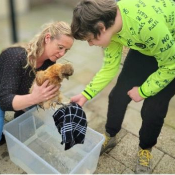 Een vrouw en een persoon met een felgroen shirt wassen een pluizige kip in een teil.