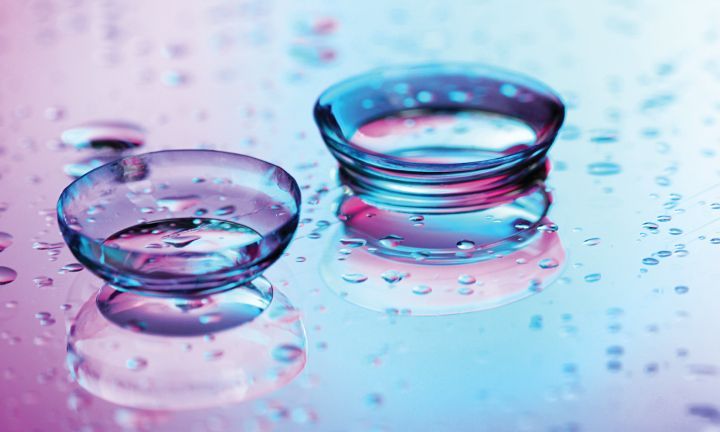 Two contact lenses are sitting on a wet surface with water drops.