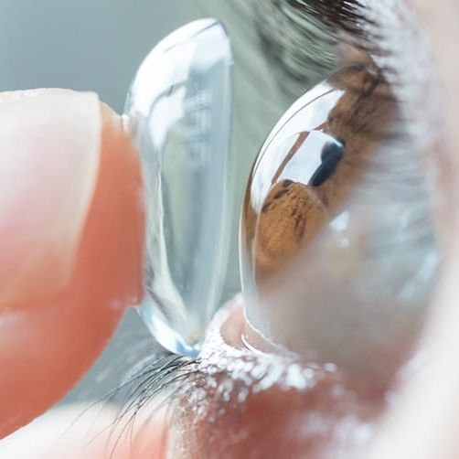 A close up of a person putting a contact lens in their eye.