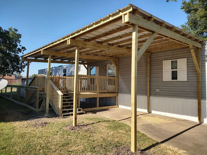 A house with a wooden deck and a carport underneath it.