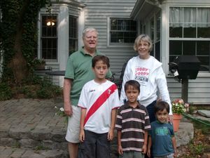Family of five poses outside a house; elderly couple and three young boys.
