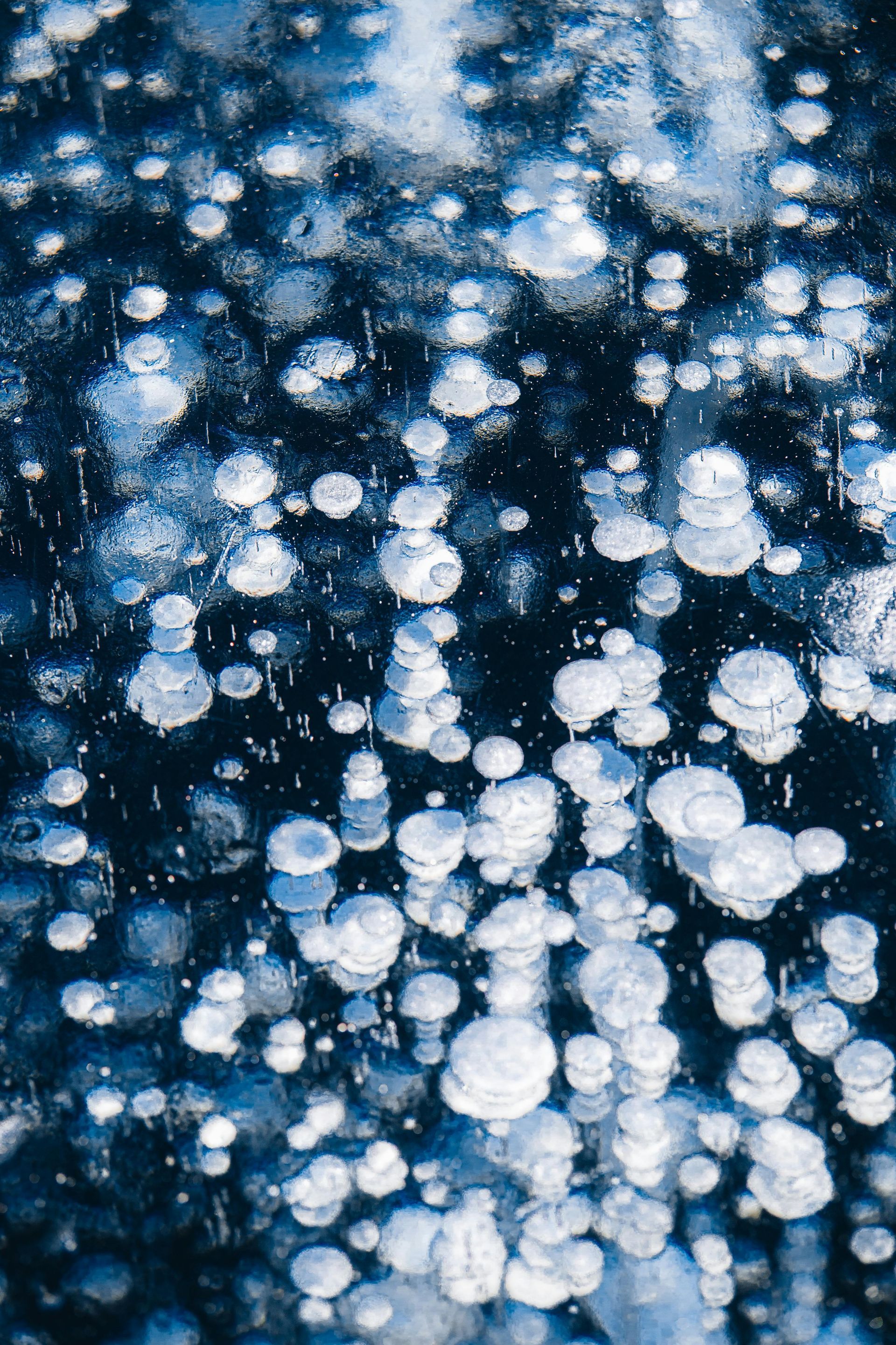 Bubbles trapped in ice, appearing blue and white against a dark background.