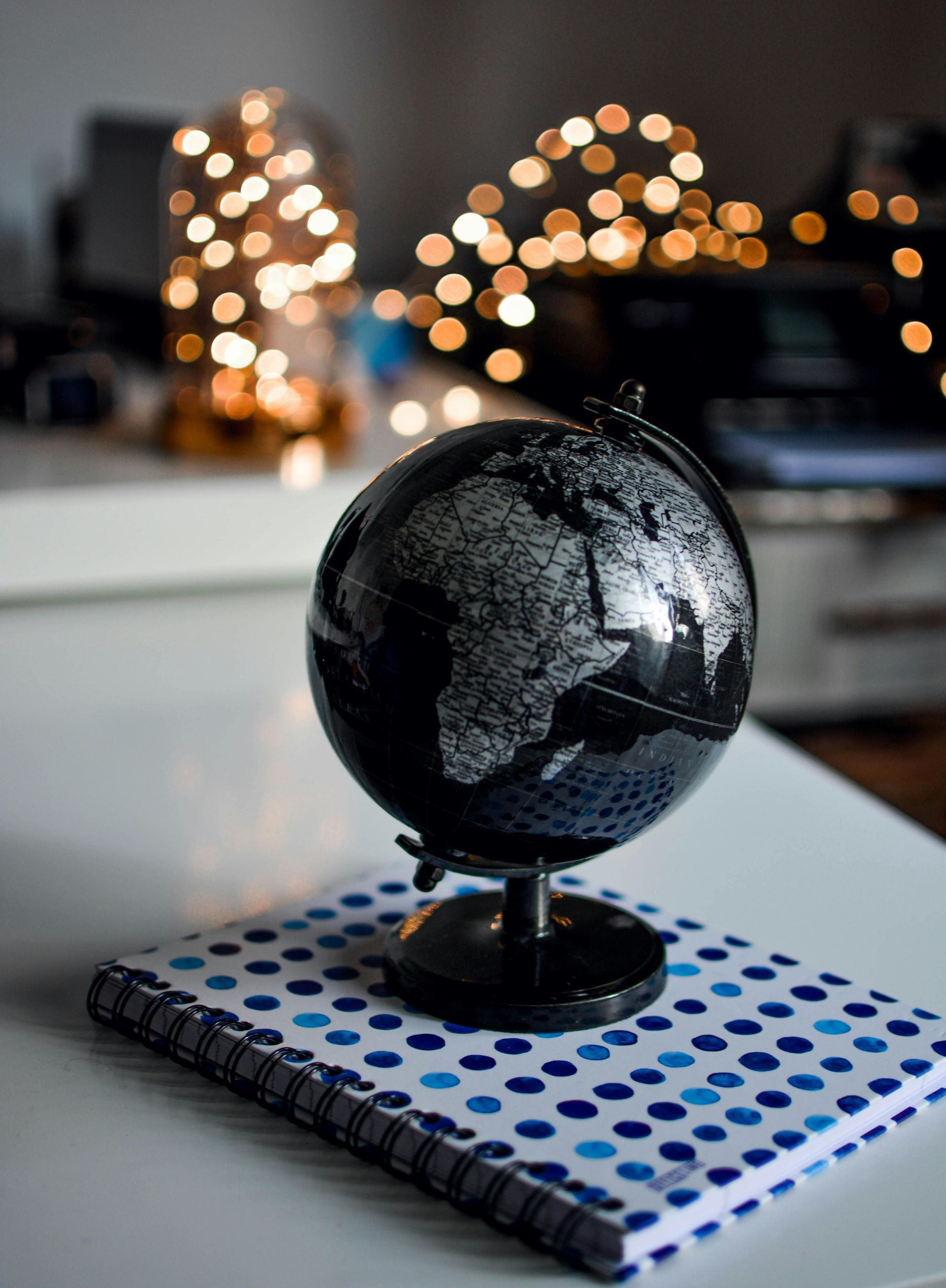 Black globe on polka-dot notebook, with blurred fairy lights in the background.