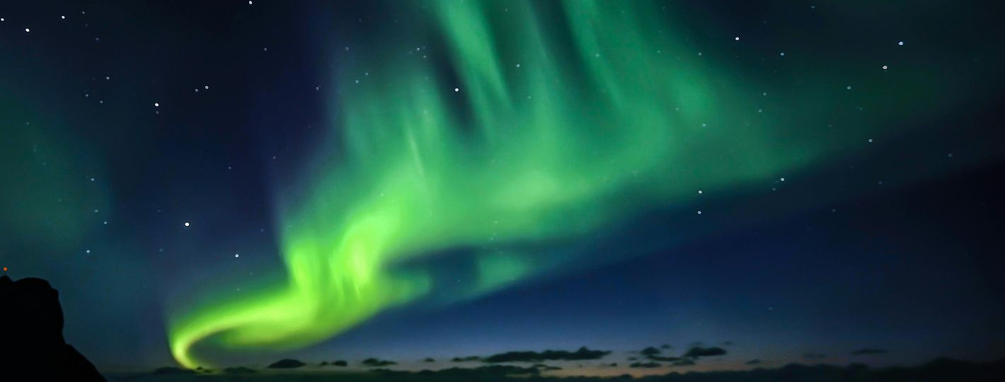 Green aurora borealis swirling in a dark night sky with visible stars.