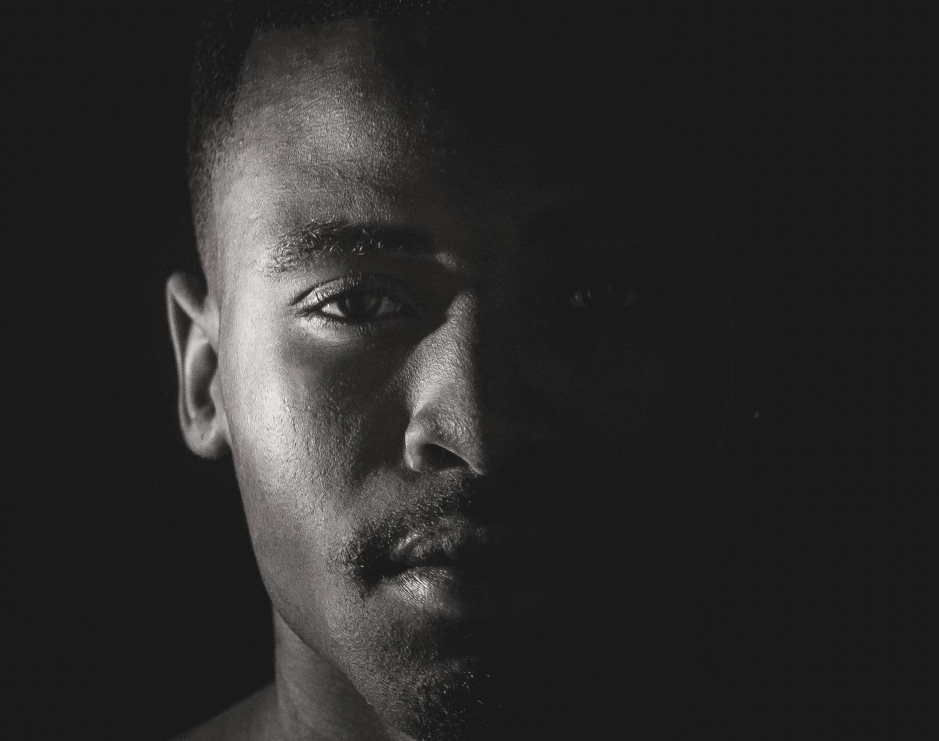 Man's face, half-lit. He looks forward with a slight frown. Dark background; close-up.