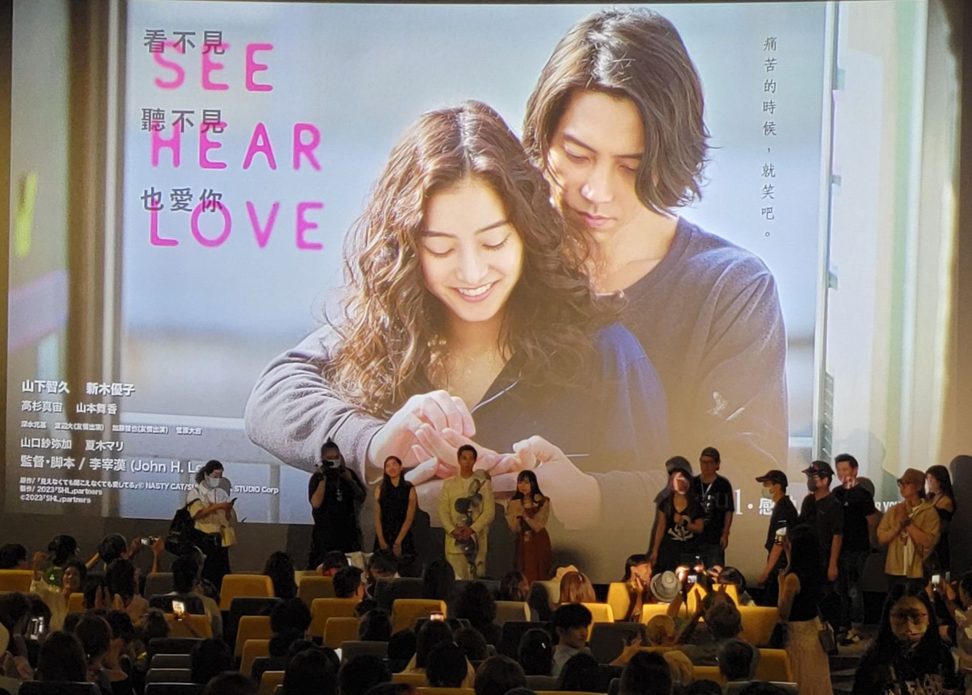 一群人坐在一個大螢幕前，上面有一個男人和一個女人的照片。