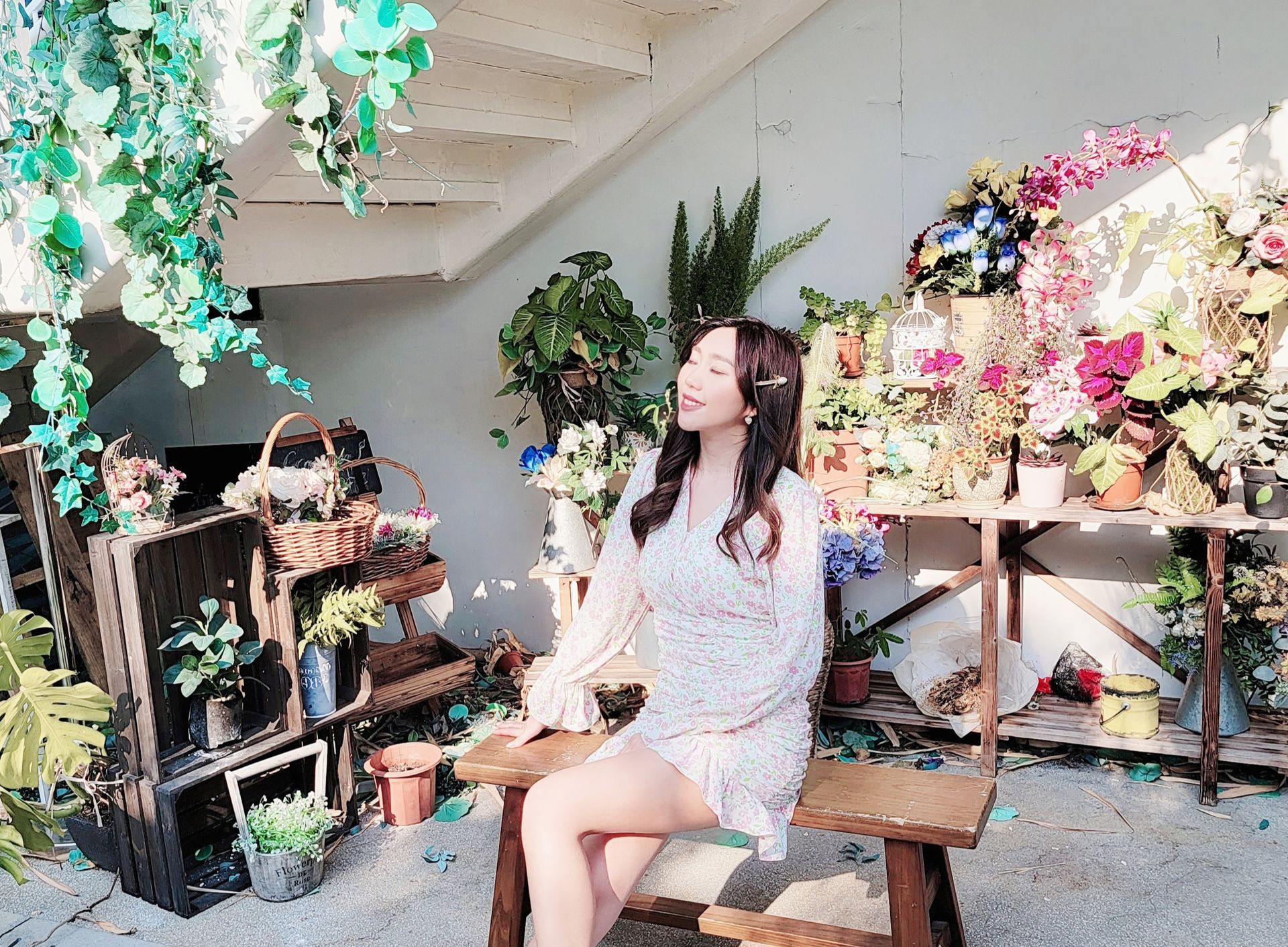 一位女士坐在鮮花展前的長椅上。