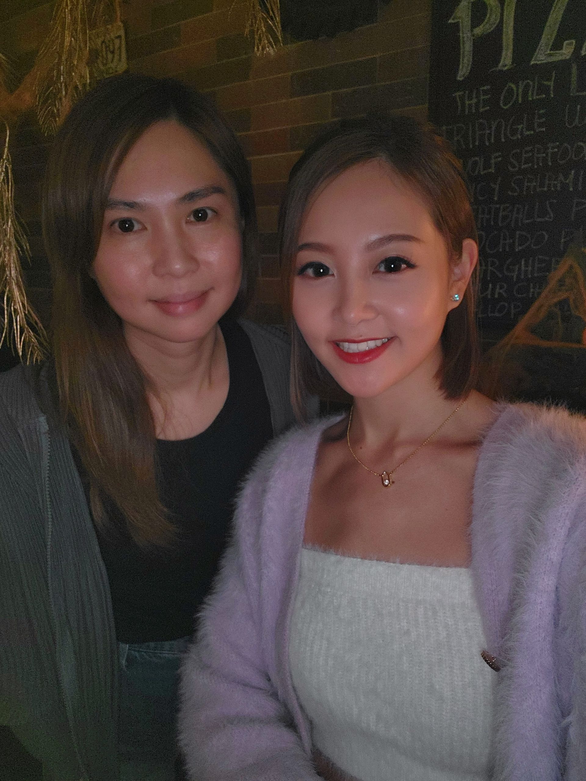 兩名女子正在擺姿勢拍照，其中一名穿著紫色毛衣