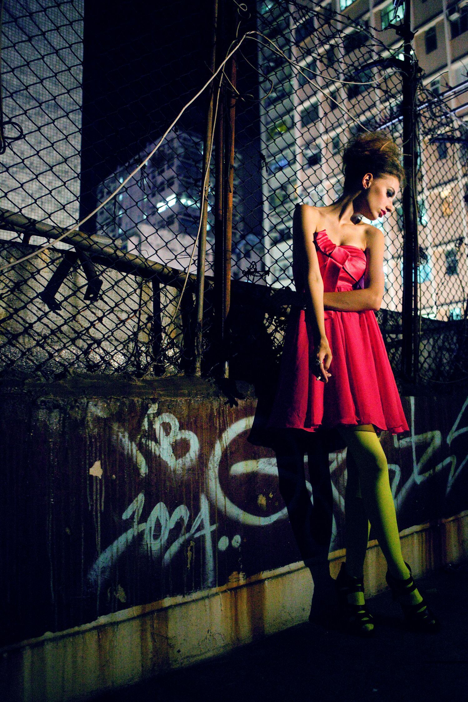 一個穿著紅色裙子的女人靠在柵欄上,柵欄上有塗鴉。
