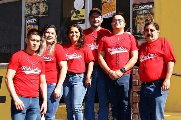 Seis personas con camisetas rojas idénticas posan juntas a la salida de un restaurante.