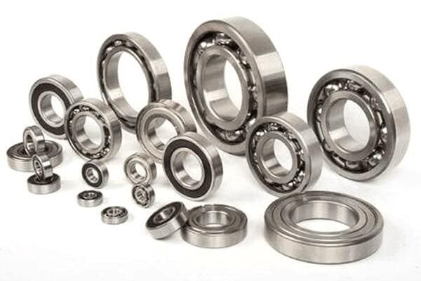 Surtido de rodamientos de bolas y anillos de rodamientos metálicos dispuestos sobre un fondo blanco.