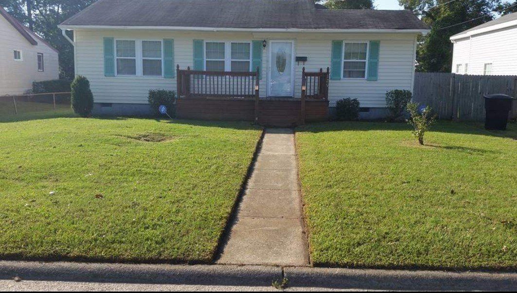 A white house with green shutters and a lush green lawn.