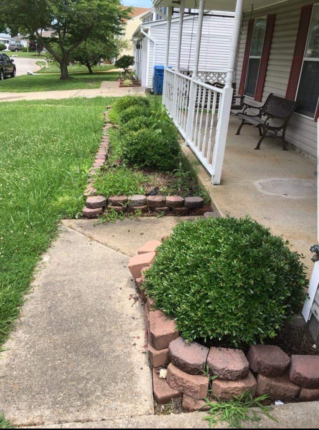 A sidewalk leading to a house with a porch and a bench.