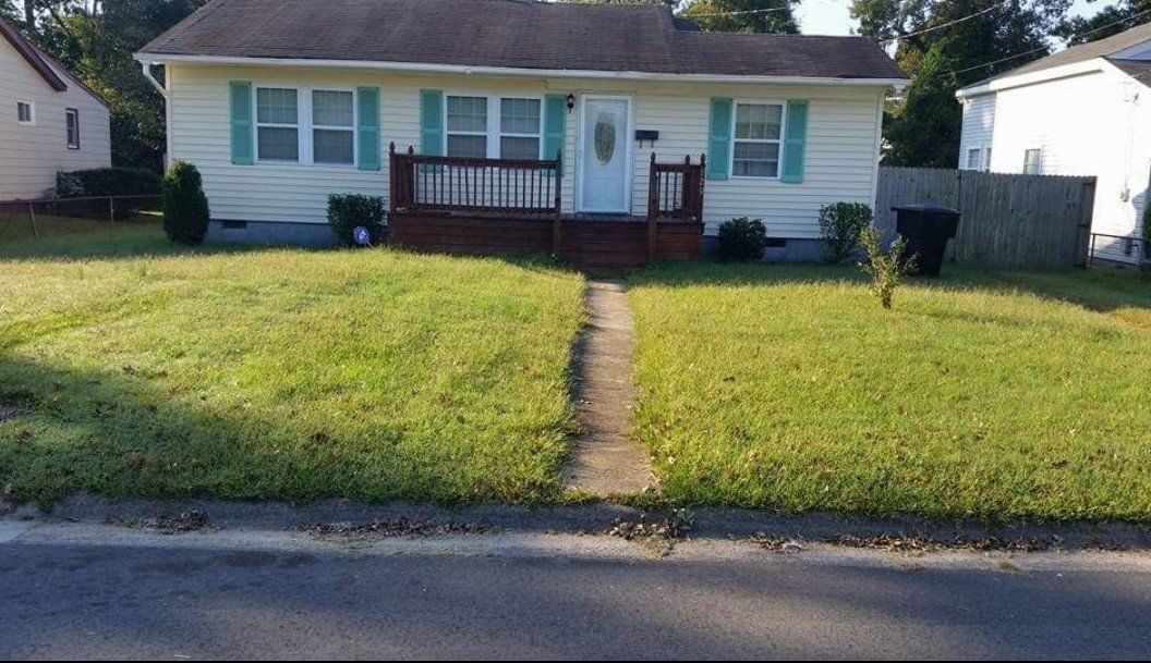 A white house with green shutters is sitting on top of a lush green lawn.