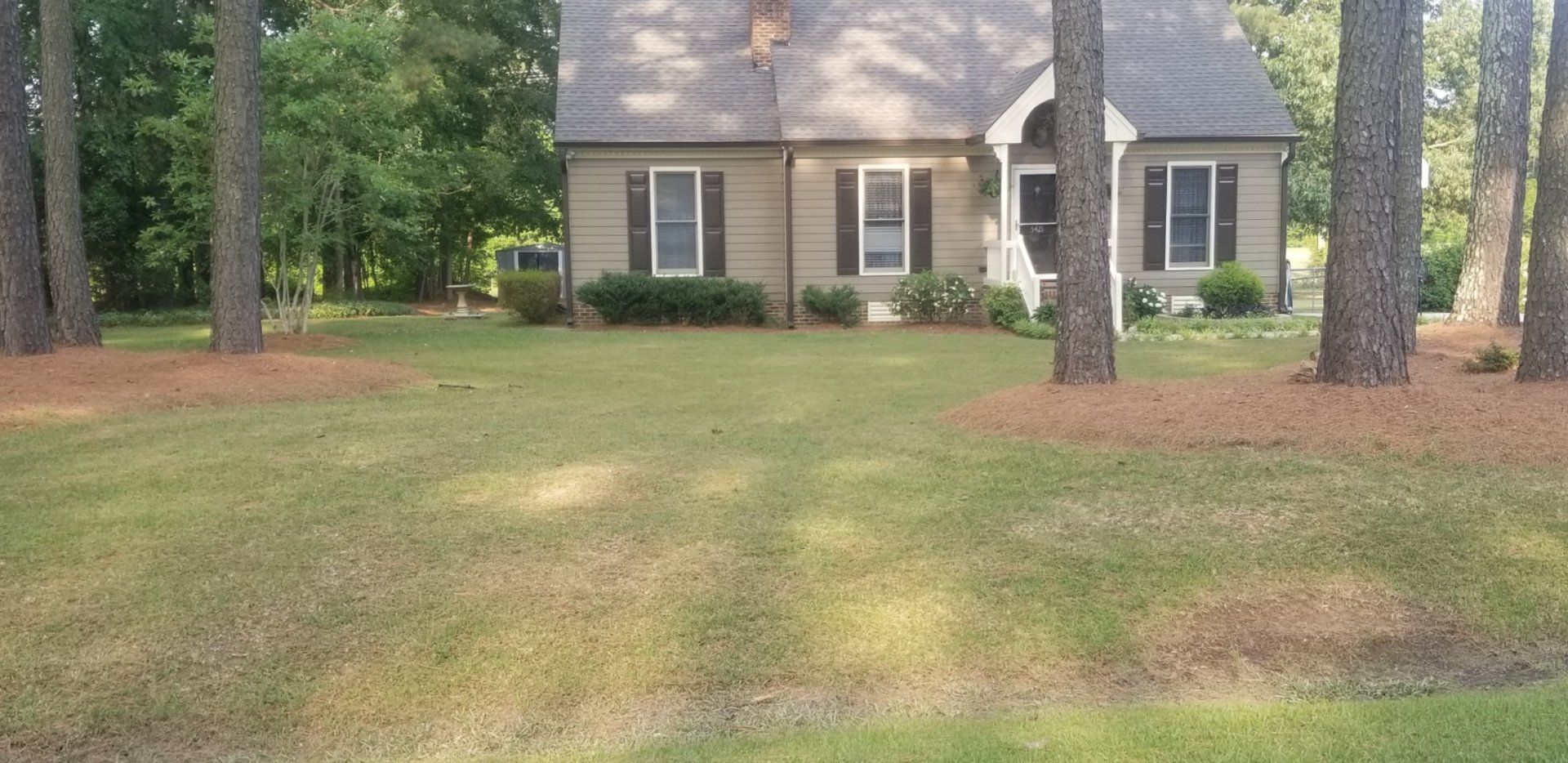 A house with a large lawn in front of it surrounded by trees.