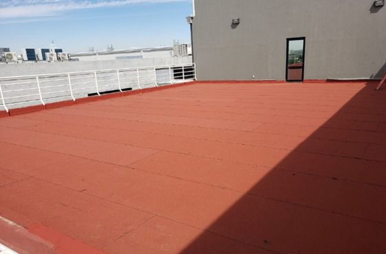 Tejado rojo con barandilla blanca y una puerta. Cielo azul claro al fondo.