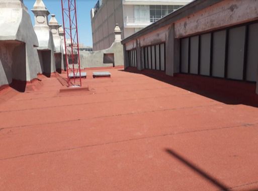 Azotea roja de un edificio con ventanas y antenas bajo un cielo azul.