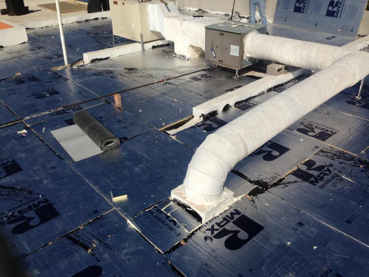 Material de techado negro con conductos de climatización en el techo de un edificio.