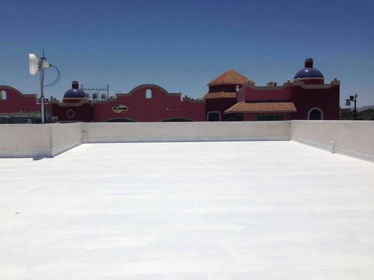Tejado blanco con edificio rojo y cúpulas azules al fondo. Cielo despejado y soleado.