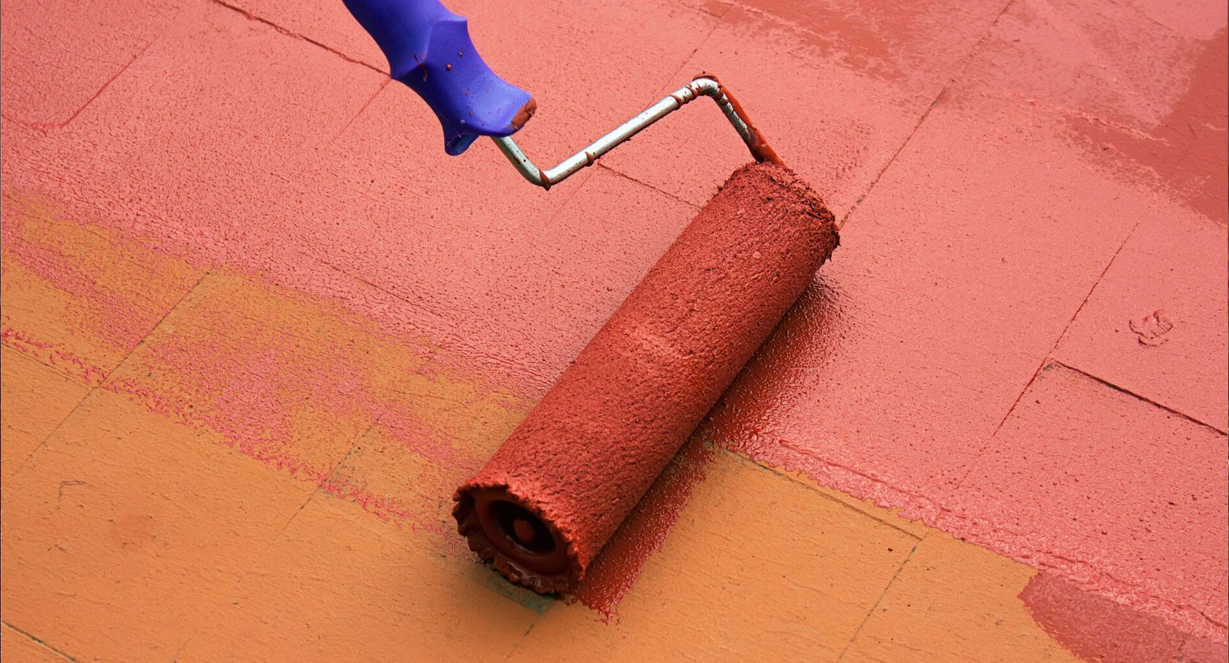 Rodillo de pintura aplicando pintura marrón rojiza sobre una superficie.