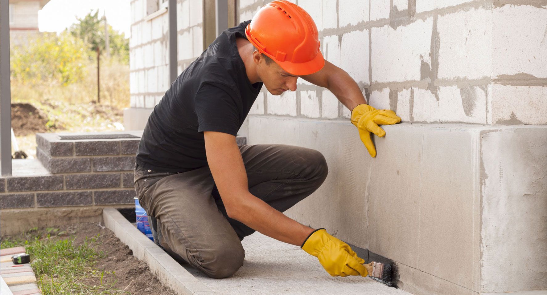 Obrero de la construcción alisando los cimientos de hormigón, con casco naranja y guantes amarillos.