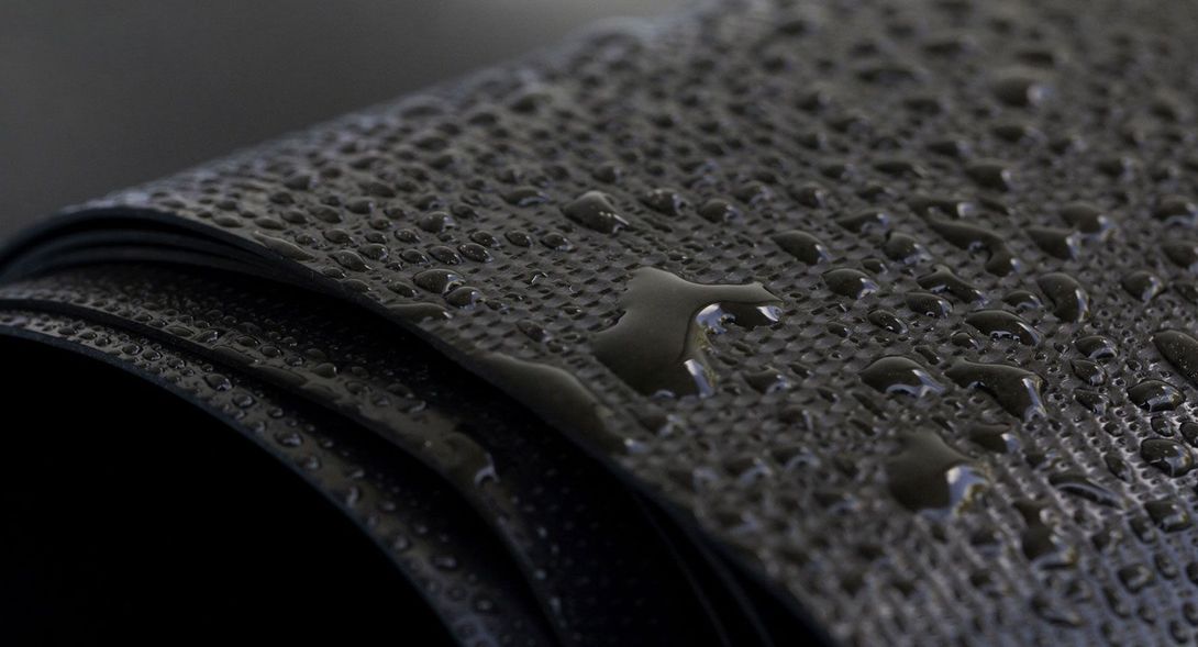 Primer plano de un material enrollado, oscuro y texturizado, cubierto de gotas de agua.