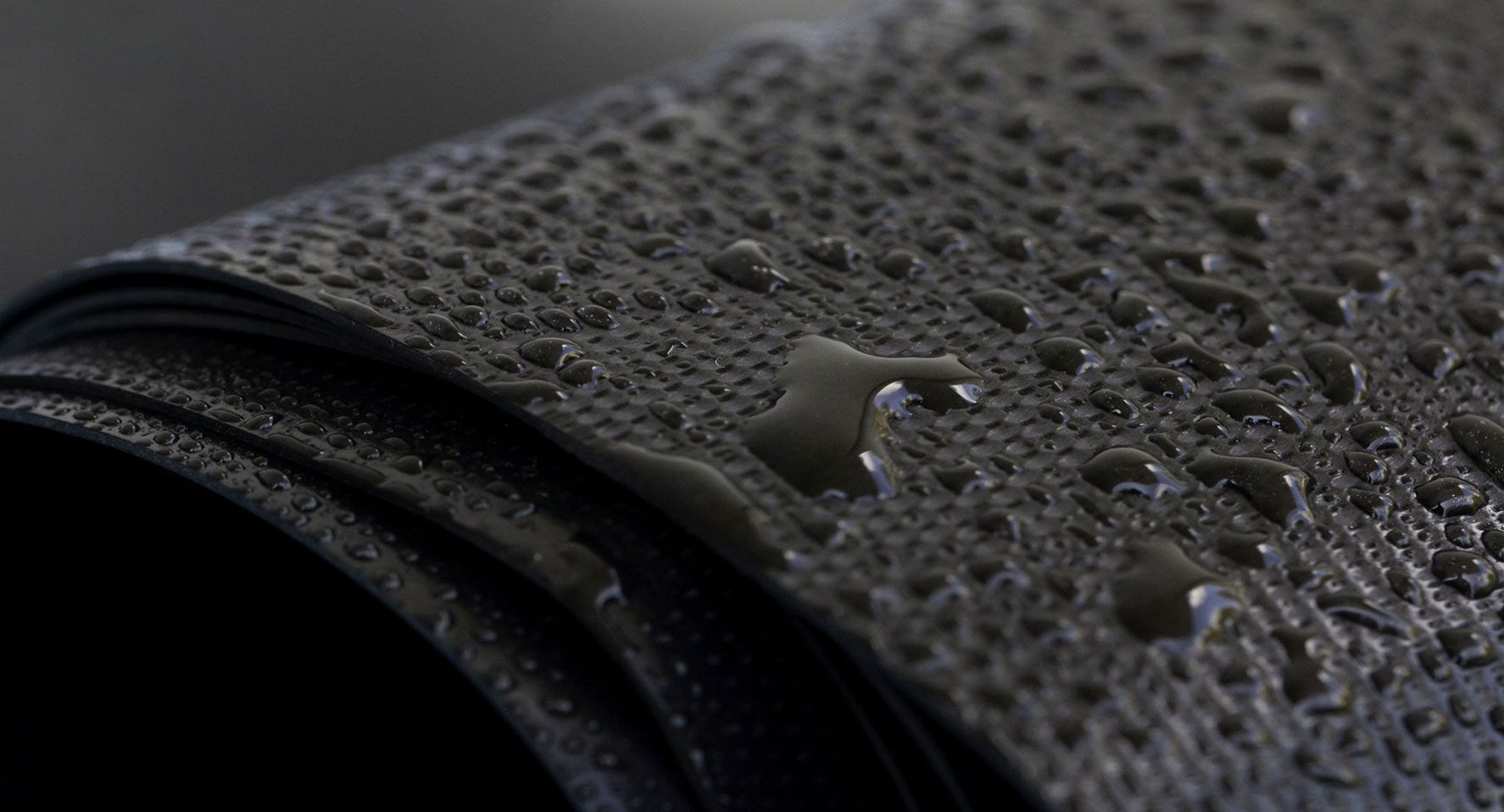 Material oscuro y texturizado enrollado, cubierto de gotas de agua.