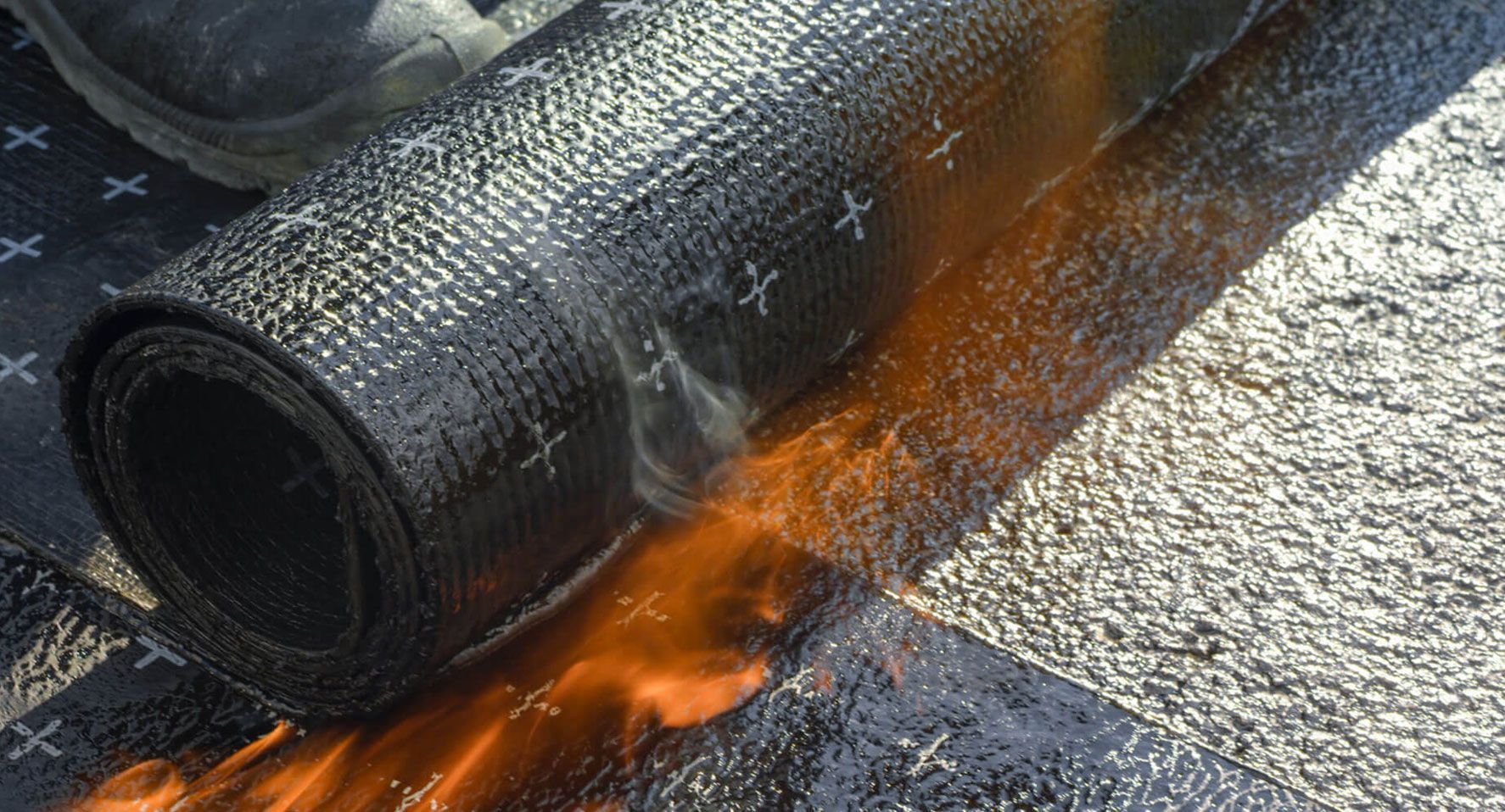 Rollo de material para techos calentándose con un soplete para su aplicación sobre una superficie texturizada.