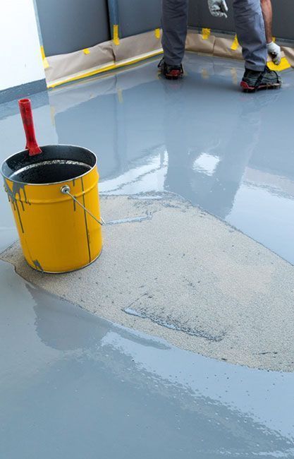 Suelo recubierto con epoxi gris; un cubo amarillo y una persona al fondo.