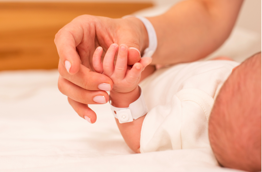 A woman is holding the hand of a newborn baby.