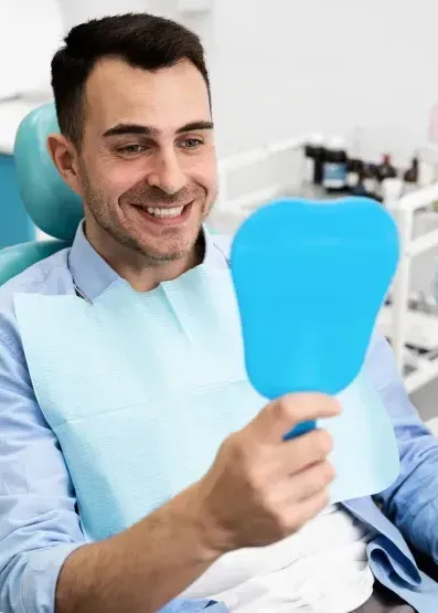 A man is sitting in a dental chair looking at his teeth in a mirror.