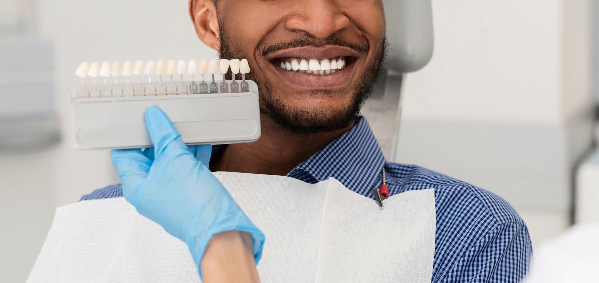 A man is sitting in a dental chair holding a box of tooth shades.