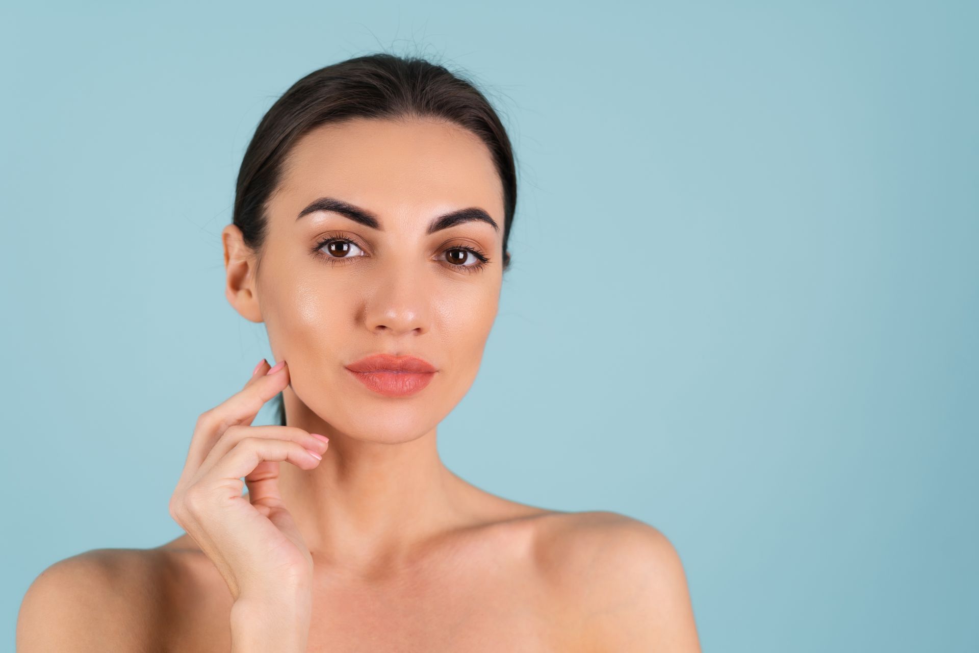 Woman with smooth skin, hand touching face, against a light blue background.