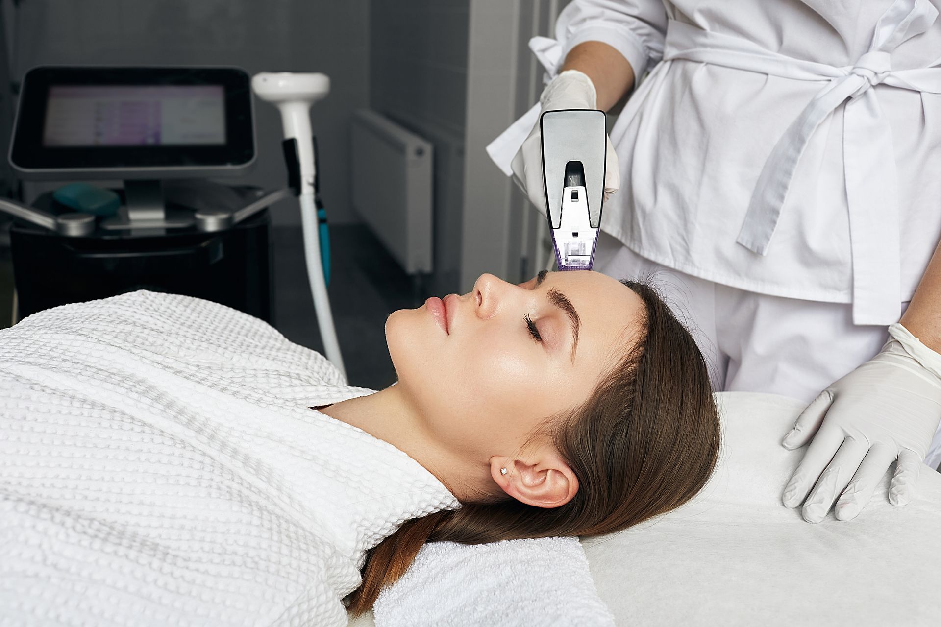 A woman is laying on a bed getting a laser treatment on her face.