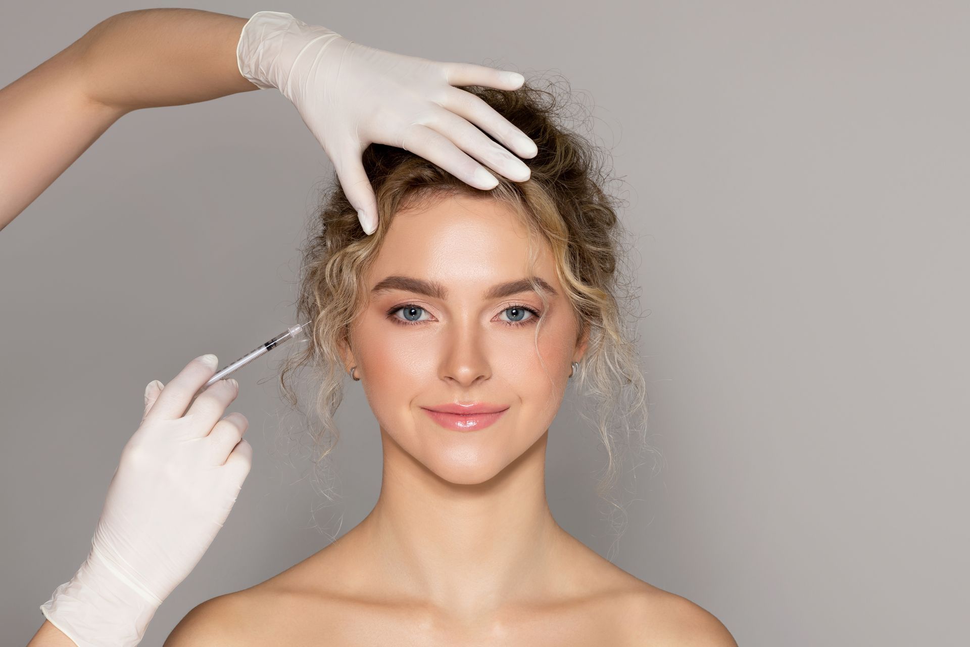 Woman receiving cosmetic injections to her forehead, smiling, doctor's gloved hands holding syringe.