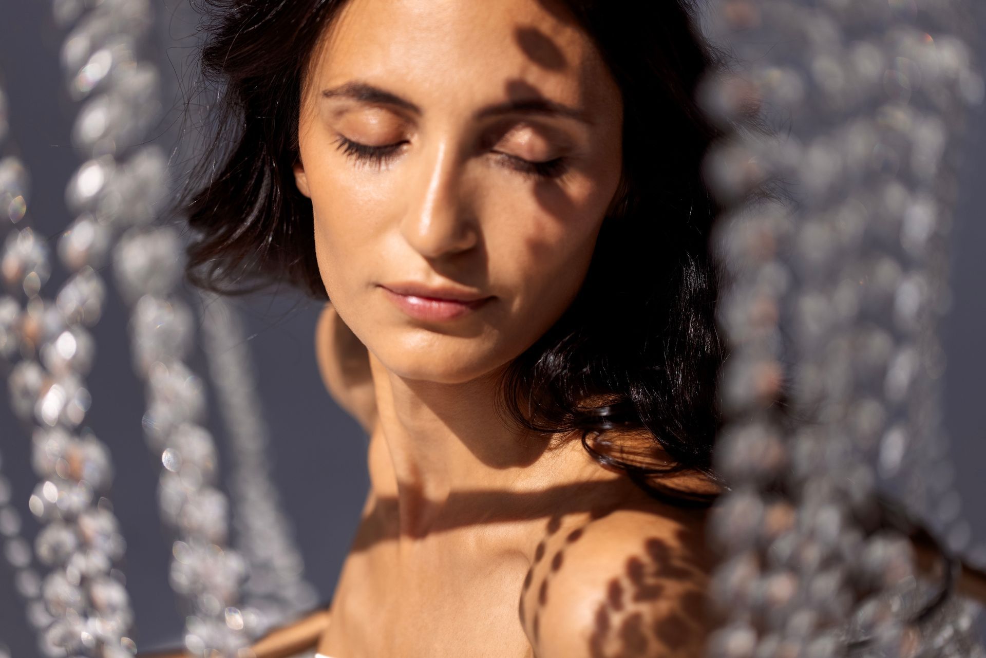 A woman is standing in front of a chandelier with her eyes closed.