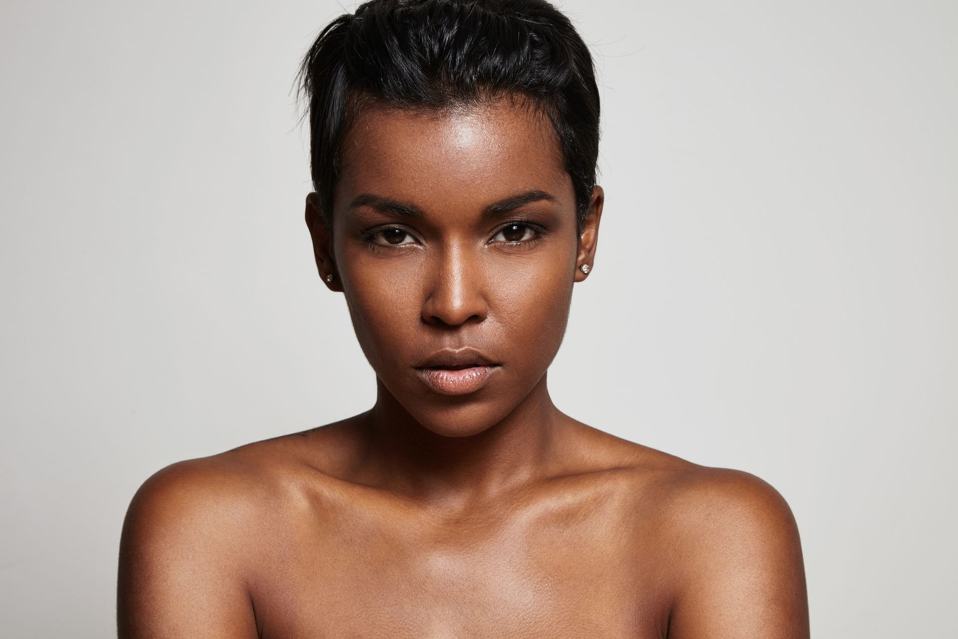 A shirtless woman with short hair is looking at the camera.