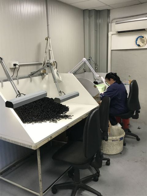 Persona al lavoro su un banco da laboratorio con un microscopio in una piccola stanza adibita a laboratorio.