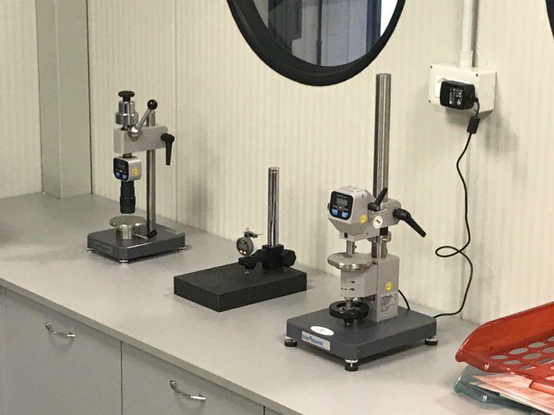 Macchine per il collaudo dei metalli su un banco da lavoro in un laboratorio o in un'officina, con una presa a muro e uno specchio nelle vicinanze.