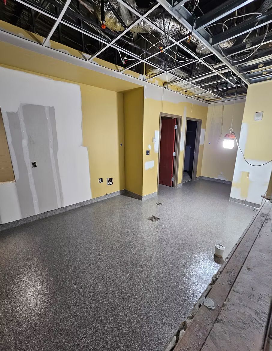 Room under construction with yellow walls, unfinished ceiling, and speckled flooring.