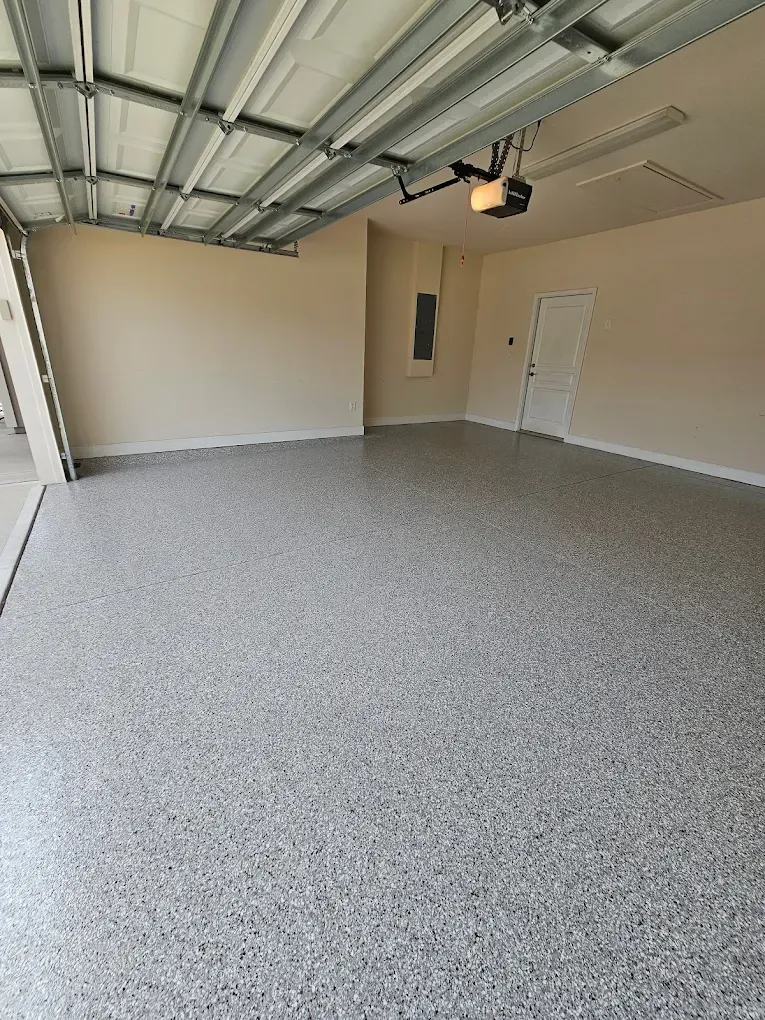 Empty garage with speckled grey floor, beige walls, and white door.