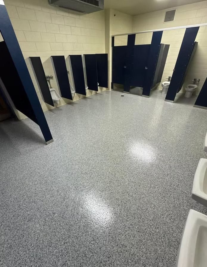 Public restroom with blue stalls, white urinals, and speckled gray flooring.