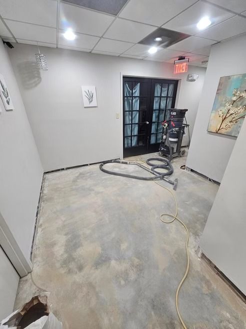 Interior room with concrete floor, black double doors, and white walls undergoing construction.