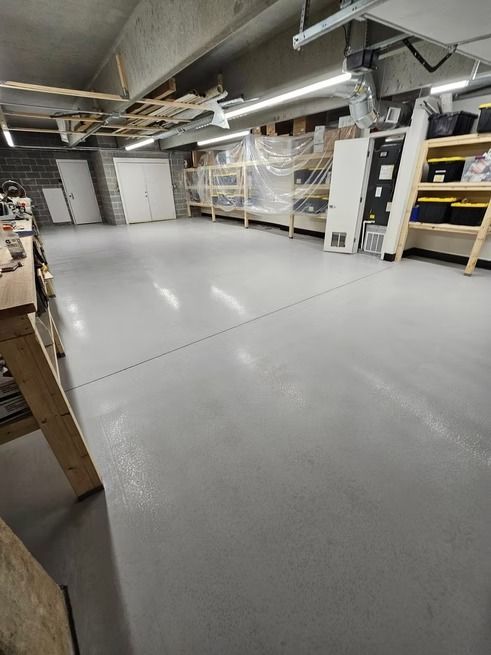 Spacious workshop with gray epoxy floor, white doors, shelving, and work benches.