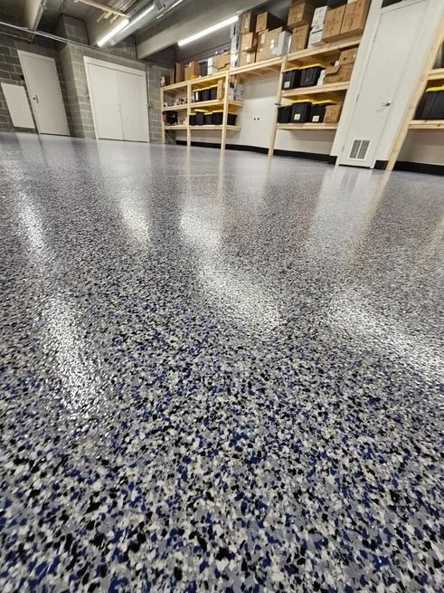 A low-angle shot of a gray, blue, and white speckled epoxy floor in a storage room with shelves and doors.