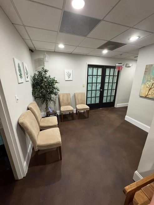 Waiting room with chairs, art, and a plant. Brown floor, white walls and ceiling. Black doors.