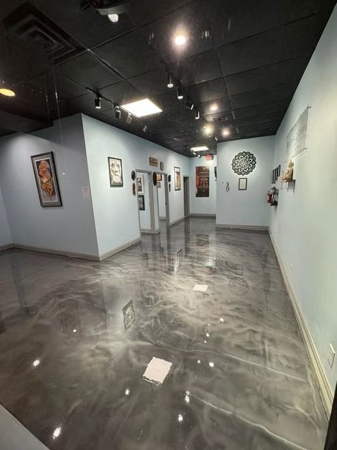 Interior of an art gallery with light blue walls, a reflective silver floor, and art on display. Black ceiling.