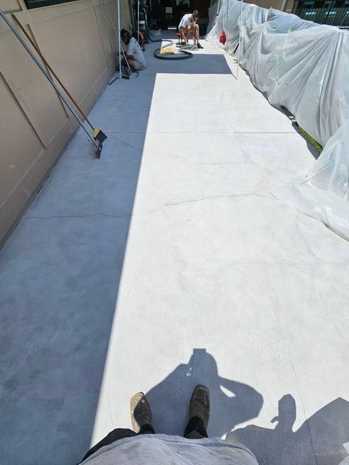 Workers applying finish to a long, light-colored concrete surface. Covered structure on right; shadow of person taking the picture in the foreground.